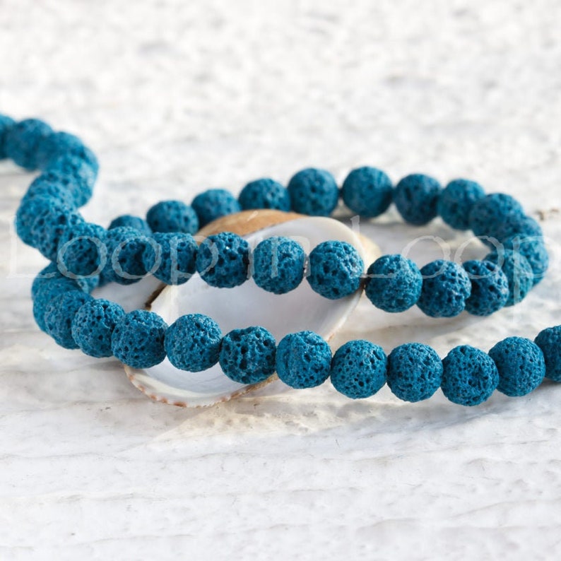 May include: A strand of teal blue lava rock beads. The beads are round and have a rough, porous texture.