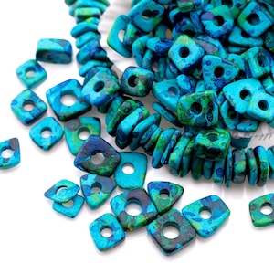 Op de afbeelding: Close-up van turquoise en blauwe vierkante kralen met een gat in het midden. De kralen hebben een gemarmerd uiterlijk met groene en donkerblauwe accenten. Sommige kralen zijn geregen, andere los.