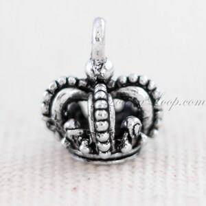 May include: Silver crown charm with a detailed design. The crown has a pointed top and a rounded base.