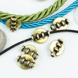 May include: Gold metal beads with a decorative design. The beads are round and have a hole in the center. They are strung on a black cord and a blue and green cord.