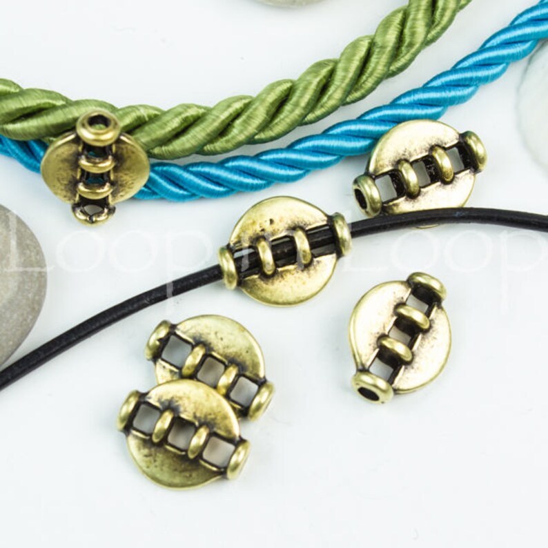 May include: Gold metal beads with a decorative design. The beads are round and have a hole in the center. They are strung on a black cord and a blue and green cord.