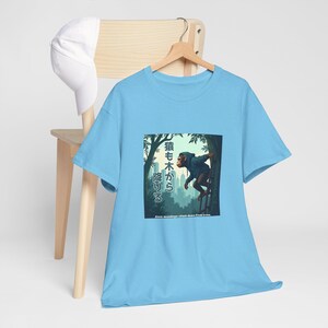 以下が含まれることがあります： 森の中で木に登る猿のグラフィックが描かれた薄い青色のTシャツ。シャツのテキストは英語と日本語で「Even monkeys climb down from trees」と書いてあります。