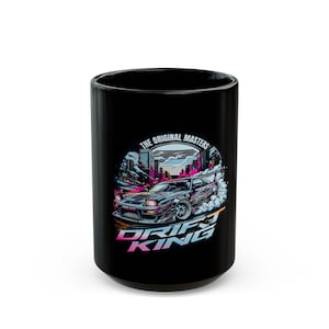 Może przedstawiać: Czarny kubek ceramiczny z grafiką samochodu dryfującego w miejskim otoczeniu. Grafika zawiera tekst "The Original Masters Drift King".