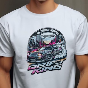 May include: White t-shirt with a graphic print of a white car drifting in a city setting. The graphic includes the text "The Original Masters" and "Drift King".