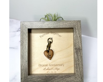 May include: A square wooden frame containing a light wood panel with the engraved text Forever Together, Bronze Anniversary, Lukas & Hope, and 10-25-26. A bronze-colored metal lobster clasp with a small wooden heart charm engraved I Love You.