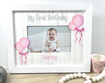 Puede incluir: Marco de fotos de madera blanca con el texto "My First Birthday" y gráficos de globos rosas. El marco contiene una foto de bebé. El nombre del bebé, "Sophia", y la fecha están impresos debajo de la foto.