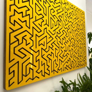 May include: A rectangular wall panel featuring a bright yellow surface with a complex, laser-cut geometric maze pattern. The design consists of interconnected lines and pathways, revealing a dark wood grain texture within the deep cutouts.