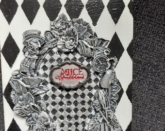 Könnte beinhalten: Eine silberne und weiße Dekorplatte mit einem schwarz-weißen Schachbrettmuster. Die Platte zeigt ein silbernes 3D-Design von Alice im Wunderland-Charakteren, darunter der Hutmacher, das weiße Kaninchen und Alice. Die Platte trägt die Worte "Alice im Wunderland" in roten Buchstaben.