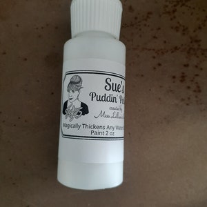 May include: A white bottle with a black and white label that reads "Sue's Puddin' Paint created by Miss Lillian". The label also says "Magically Thickens Any Water Paint 2 oz".