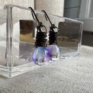 May include: A pair of iridescent glass teardrop earrings with a copper wire wrap and silver hooks.