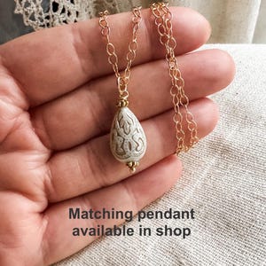 May include: A gold chain necklace with a white pearlescent pendant featuring a detailed etched design.  Matching pendant available in shop.