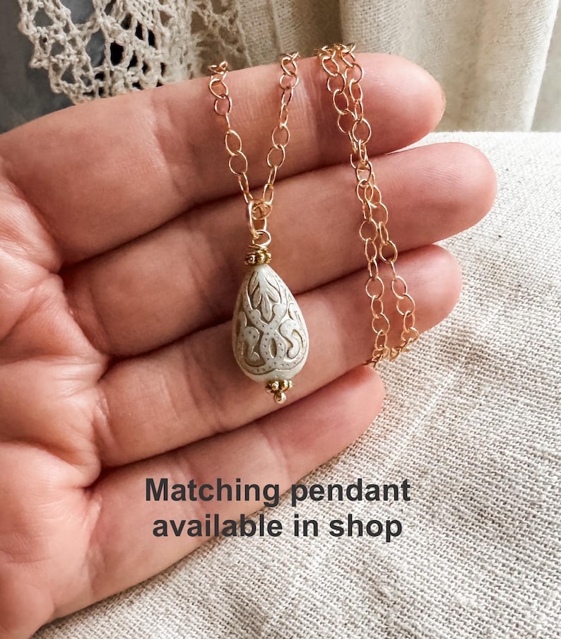 May include: A gold chain necklace with a white pearlescent pendant featuring a detailed etched design.  Matching pendant available in shop.