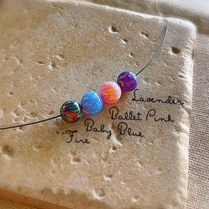 Pu&ograve; includere: Primo piano di cinque perline di vetro colorate infilate su un filo. Le perline sono etichettate "Fire", "Baby Blue", "Ballet Pink" e "Lavender".