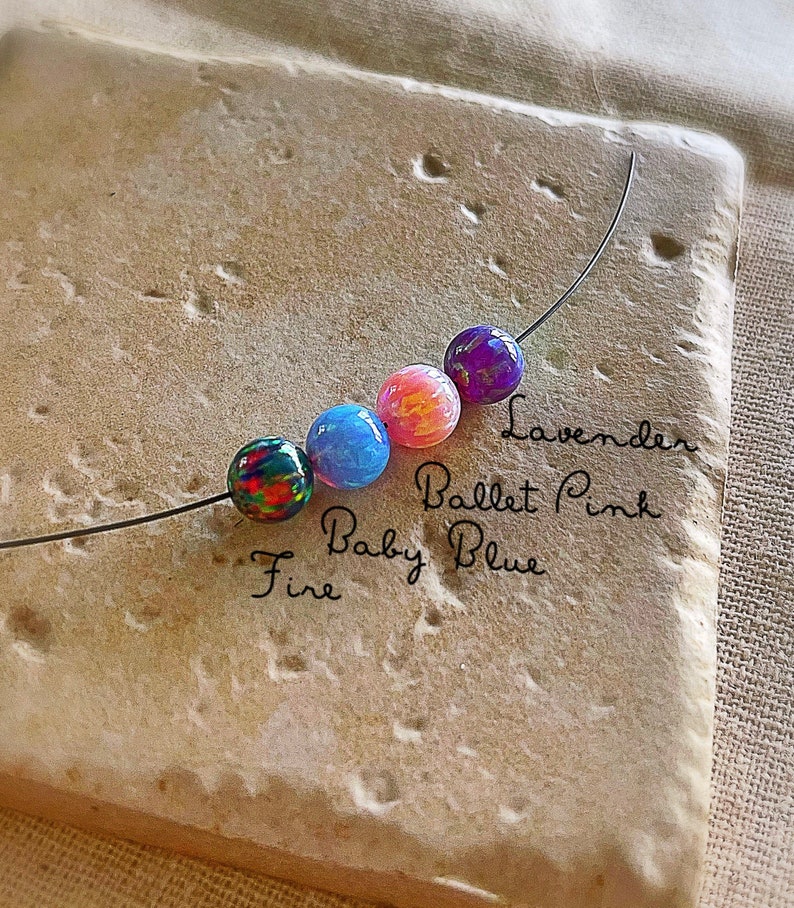 Pu&ograve; includere: Primo piano di cinque perline di vetro colorate infilate su un filo. Le perline sono etichettate "Fire", "Baby Blue", "Ballet Pink" e "Lavender".