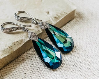 May include: A pair of silver teardrop earrings with blue and green crystal accents. The earrings have a delicate design and are perfect for a special occasion.