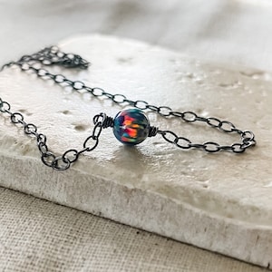 Pu&ograve; includere: Una delicata collana a catena nera con un unico ciondolo di opale iridescente.