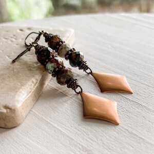 May include: A pair of long, dangle earrings with copper-colored metal accents and brown, green, and white gemstone beads.