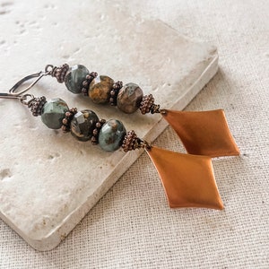 May include: A pair of long, dangle earrings with green and brown jasper beads and copper diamond-shaped charms.