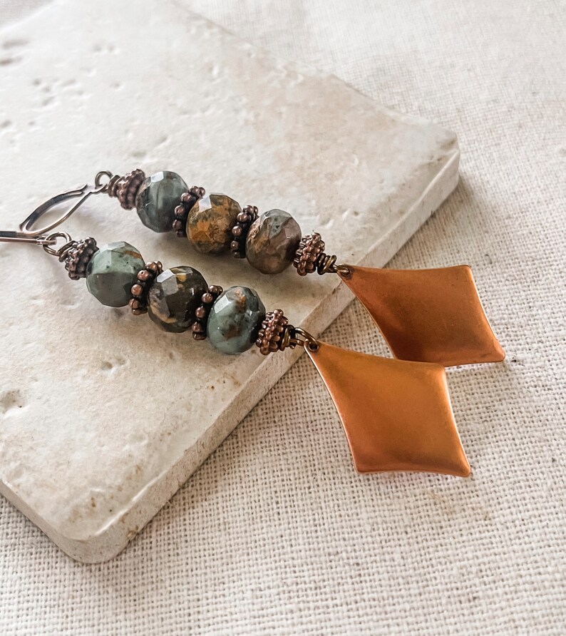 May include: A pair of long, dangle earrings with green and brown jasper beads and copper diamond-shaped charms.