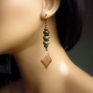 May include: A pair of long, dangle earrings with a copper-toned, diamond-shaped pendant and green and brown beads.