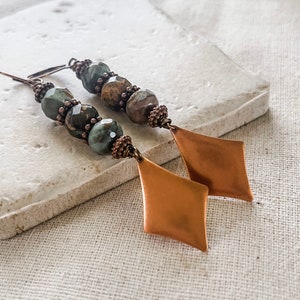 May include: A pair of long, dangle earrings with copper-toned diamond-shaped charms and green and brown gemstone beads.