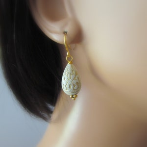 May include: White teardrop-shaped earrings with gold filigree detailing and a gold hook closure.