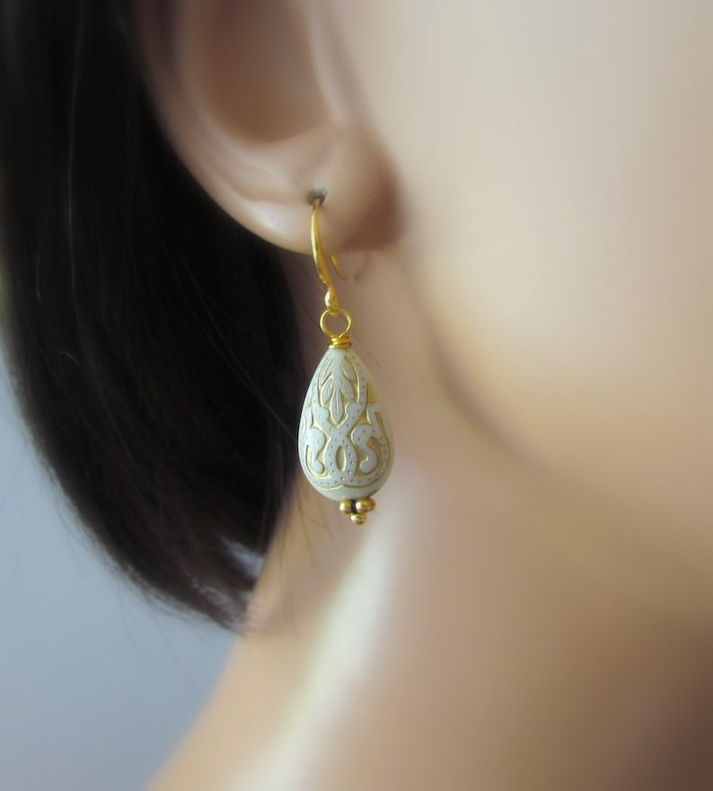 May include: White teardrop-shaped earrings with gold filigree detailing and a gold hook closure.