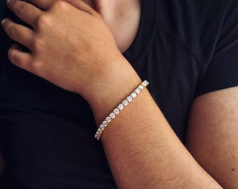 May include: A gold bracelet with multiple round, clear gemstones. The bracelet is worn on a person's wrist, with the arm and hand visible. The background is a black shirt.