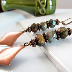 May include: A pair of long, dangle earrings with copper diamond-shaped charms and green and brown gemstone beads.