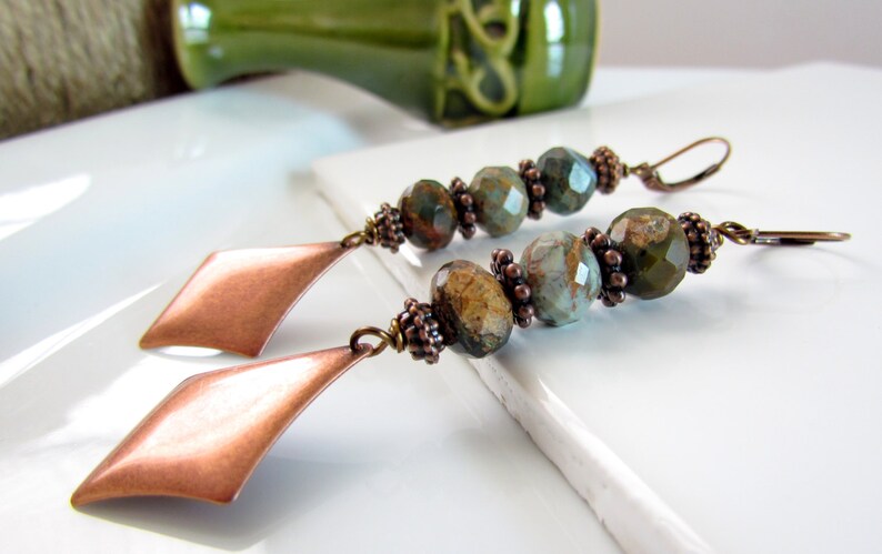 May include: A pair of long, dangle earrings with copper diamond-shaped charms and green and brown gemstone beads.