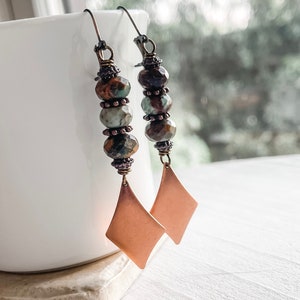 May include: A pair of dangle earrings with copper-toned diamond-shaped charms and brown, green, and blue gemstone beads.
