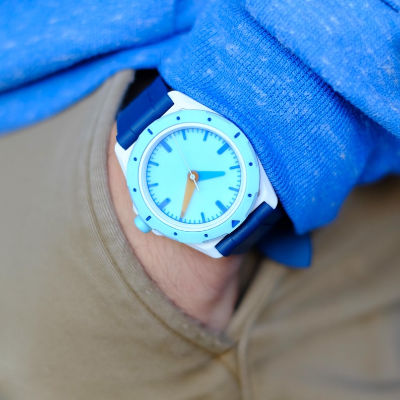 May include: A white wristwatch with a blue face and blue and white hands. The watch has a blue strap.