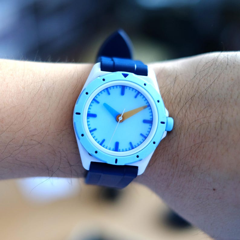 May include: A white and blue wristwatch with a blue face and orange second hand. The watch has a blue rubber strap.