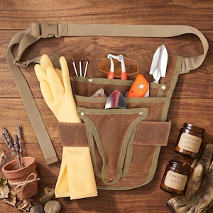 May include: A brown gardening tool belt with multiple pockets, filled with tools, yellow gloves, and a tan strap. The belt includes a trowel, hand rake, pruning shears, and a small orange tool. Two jars of garden seeds and a small terracotta pot are also visible.