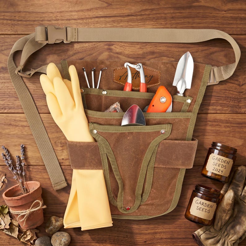 May include: A brown gardening tool belt with multiple pockets, filled with tools, yellow gloves, and a tan strap. The belt includes a trowel, hand rake, pruning shears, and a small orange tool. Two jars of garden seeds and a small terracotta pot are also visible.