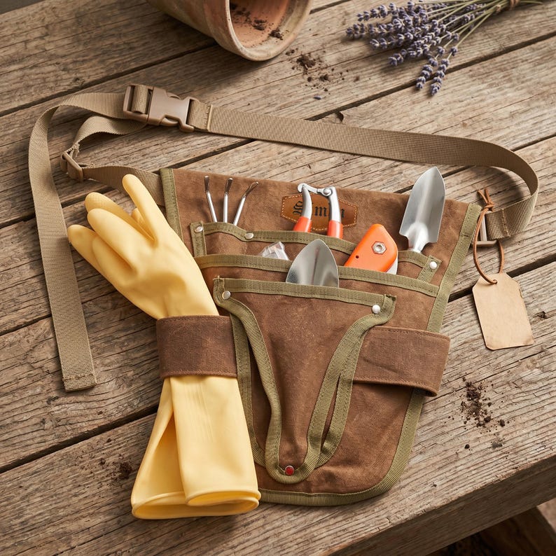 May include: A brown canvas gardening tool belt with multiple pockets, holding various gardening tools, including a trowel, hand rake, and pruning shears. A pair of yellow gardening gloves is tucked into the belt. The belt has a tan strap and buckle.