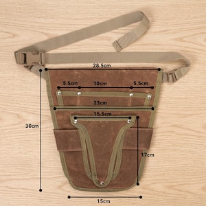 May include: A brown canvas tool belt with a beige adjustable strap and buckle. The belt has multiple pockets and is 11.8 inches tall, 5.9 inches wide, and 9 inches deep. The belt's strap is 11.2 inches long.