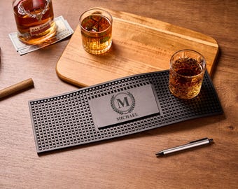 May include: A bar setup with a bottle of liquor, two glasses of amber liquid, and a cigar. A black bar mat with a personalized nameplate that reads "MICHAEL" is in the center. A wooden cutting board and a pen are also present.