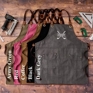 May include: A collection of canvas aprons in various colors: army green, red, coffee, black, and dark grey. Each apron features leather straps, pockets, and a personalized golf-themed design with the name "JIMMY".