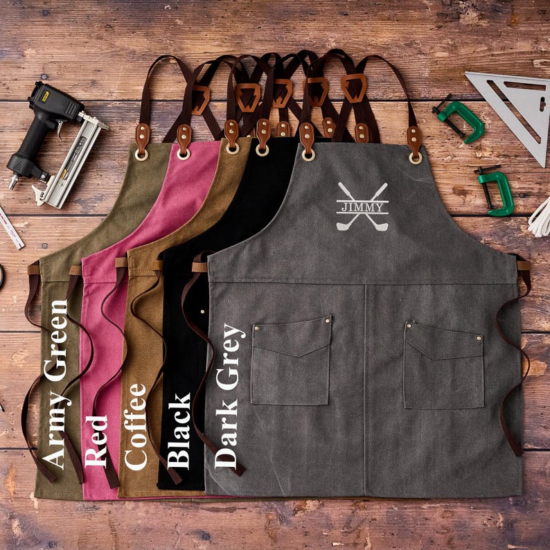 May include: A collection of canvas aprons in various colors: army green, red, coffee, black, and dark grey. Each apron features leather straps, pockets, and a personalized golf-themed design with the name "JIMMY".