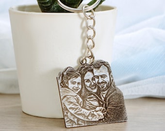 Puede incluir: Un llavero de plata con una foto grabada rectangular de una familia de tres. La foto muestra a un hombre, una mujer y un niño, todos sonriendo.