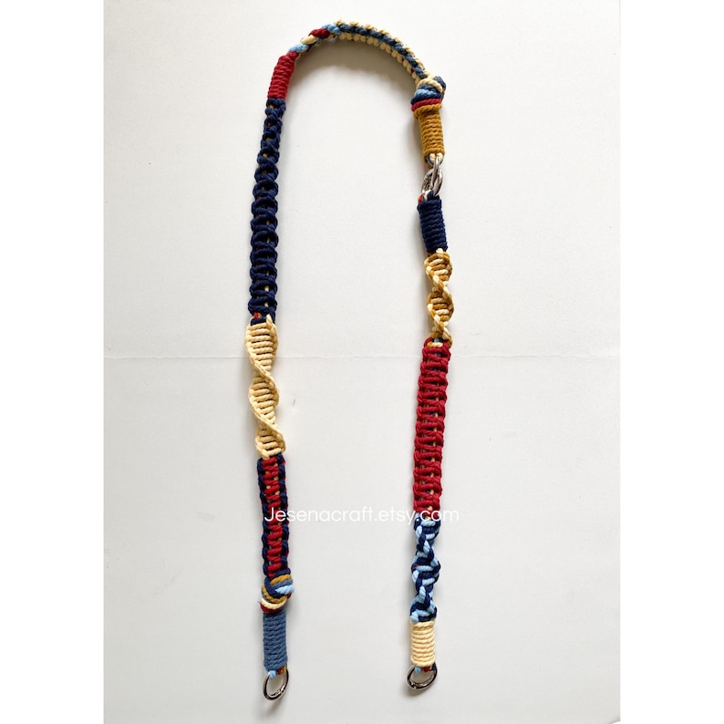 May include: A macrame strap in a U-shape, featuring a mix of colors including navy blue, red, beige, and gold. The strap has a DNA-like design and is finished with metal clasps. The text "Jesenacraft.etsy.com" is visible.