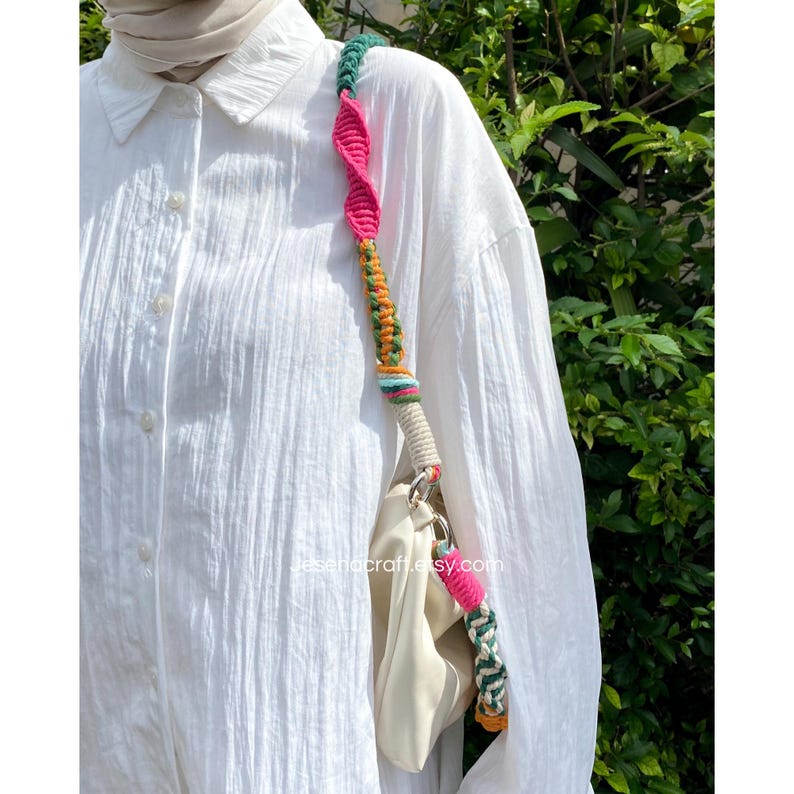 May include: A cream-coloured handbag with a vibrant macrame strap. The strap incorporates a spiral pattern with pink, green, orange, and blue hues. The bag has silver hardware. The Etsy shop name, jesenacraft.etsy.com, is visible.