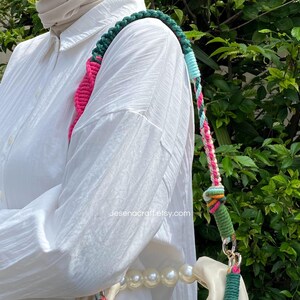 May include: A multi-coloured crochet shoulder strap for a handbag. The strap has a green, pink, blue, and white braided design. The bag is white with a pearl strap. The text "Jesenacraft.etsy.com" is visible.