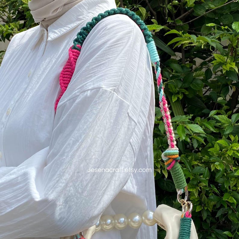 May include: A multi-coloured crochet shoulder strap for a handbag. The strap has a green, pink, blue, and white braided design. The bag is white with a pearl strap. The text "Jesenacraft.etsy.com" is visible.