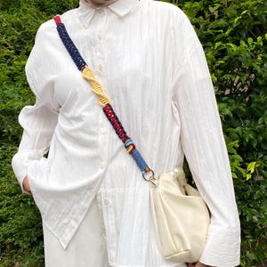 May include: A cream-colored handbag with a colorful macrame strap. The strap features blue, red, and yellow woven sections. The bag is worn over the shoulder. The website address Jesenacraft.etsy.com is visible on the image.