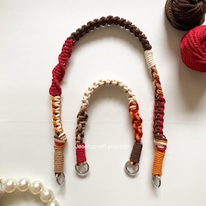 May include: Two macrame bag handles in shades of brown, red, orange, and cream. The larger handle is arched, with a spiral design in the middle. The smaller handle is a smaller version of the larger one. Both have silver metal rings.