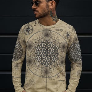 May include: Beige long-sleeve shirt featuring a geometric design with compass rose and Metatron's Cube patterns. The shirt has a vintage map-like aesthetic. The design is in shades of gray and black.