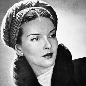 May include: A black and white photo of a woman wearing a turban-style hat with a crocheted design. The hat is decorated with small white beads. The woman is wearing a fur collar and looking to the right. The photo is from a vintage magazine and includes the text "No. 2779 Page 6".
