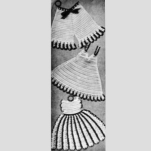 Puede incluir: Una colección de artículos de ganchillo hechos a mano, que incluyen dos agarraderas con un lazo negro, una agarradera con forma de vestido y una agarradera con forma de vestido a rayas. Cada artículo presenta una base blanca con ribete negro y presillas para colgar.